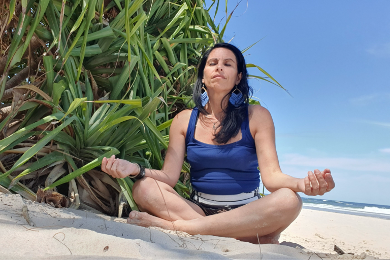 Veronica Galipo, life coach and self-love guide, sitting peacefully on coastal rocks