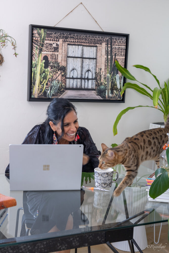 "Veronica Galipo, life coach and self love guide, laughing with her cat while working at her laptop at home.